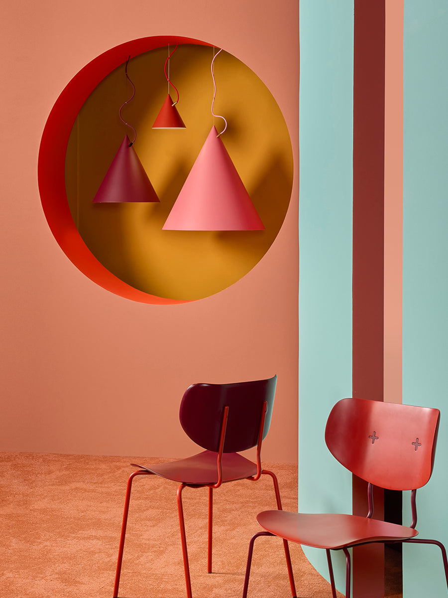 Two red cone-shaped pendant lights hanging above two red chairs against a colorful wall.